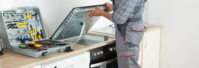 Cooktop repair technician lifting a built-in stovetop for service in Tampa, FL