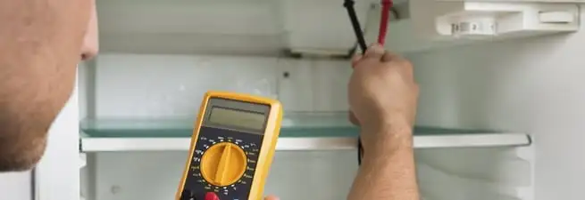 Refrigerator repair technician testing electrical components with a multimeter in Tampa, FL